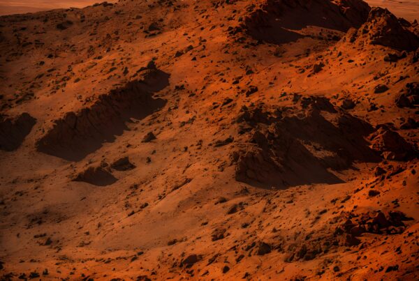 Desert landscape with rugged terrain, vibrant orange, and clear sky.