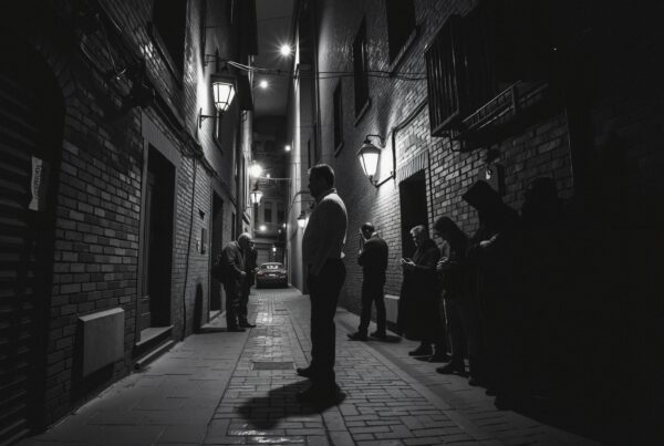 Black and white photo of people standing in a narrow alley with lanterns casting dramatic shadows.