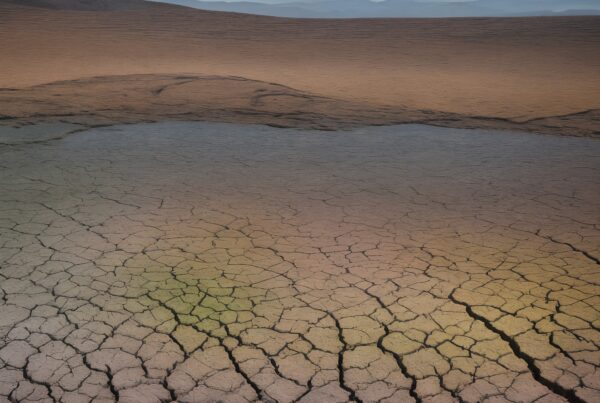 A sprawling cracked desert landscape with distant mountain silhouettes at sunset.