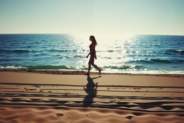 A woman walks along a sandy beach at sunset with shimmering ocean waves in the background.