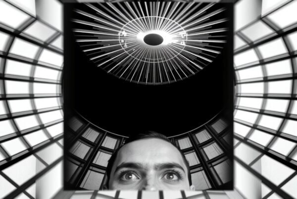 Surreal black and white photo of a man gazing up at a radial light inside a geometric structure.