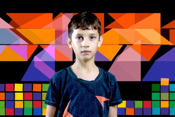 A young boy stands before a vibrant geometric background, showcasing colorful abstract shapes.