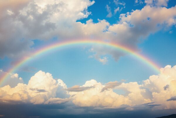 A vibrant rainbow arcs across a blue sky with fluffy clouds.