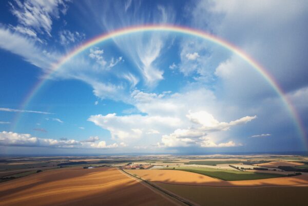 A vibrant rainbow arches over a panoramic rural landscape.