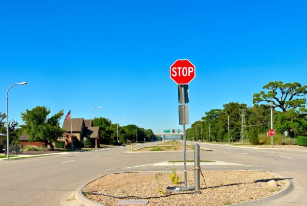 A quiet suburban street with a prominent stop sign under a bright blue sky.