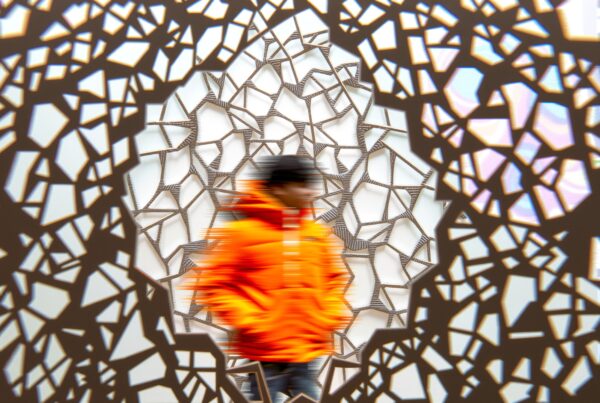 Person in orange jacket, standing against a geometric patterned background.