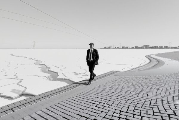 A man in a suit walks along a brick promenade with a frozen landscape and city skyline in the background.