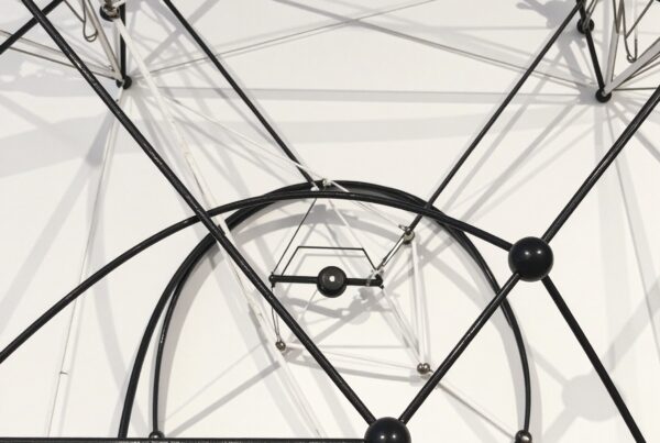 Intricate geometric metal structure with intersecting rods and cables casting complex shadows on a white background.
