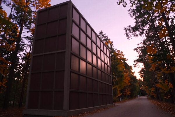 An imposing rectangular building stands under a colorful autumn sky, surrounded by trees.