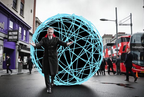 A man with a glowing blue spherical structure on a city street with double-decker buses and purple storefronts.
