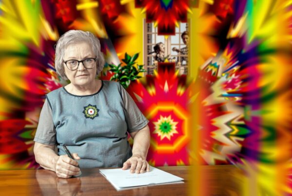 Elderly woman writing at a table with vibrant, psychedelic background.