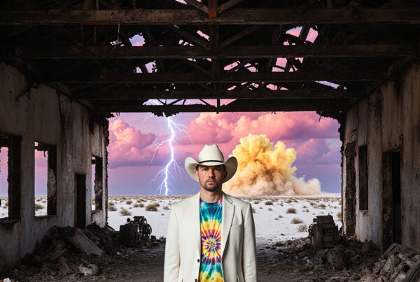 A man in a tie-dye shirt and cowboy hat stands in a dilapidated building with a dramatic desert and lightning backdrop.