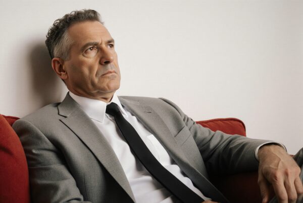 Businessman in gray suit deep in thought on a red sofa.