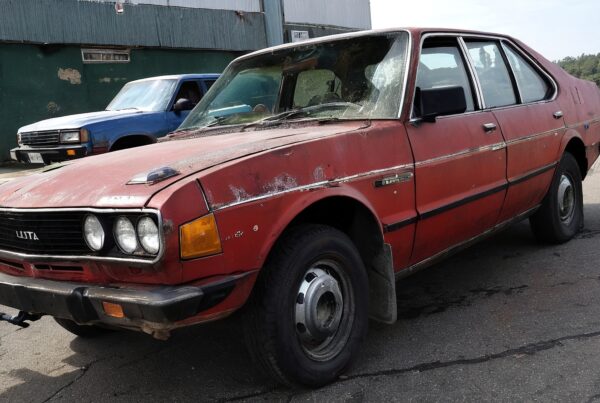 Old red sedan parked on street, showing rust and wear.