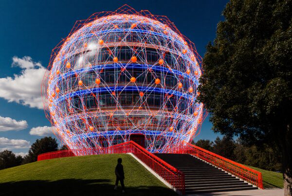 A futuristic spherical structure with neon lights and red stairs against a blue sky.