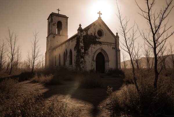 "Sepia-toned image of an abandoned church with sunlit halo, surrounded by barren trees and ivy."