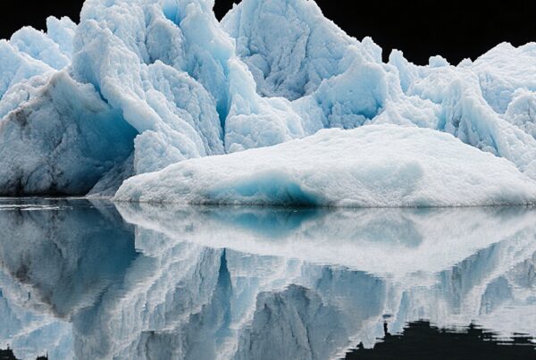 A towering blue iceberg reflecting in calm, dark waters, creating a dramatic and serene natural scene.