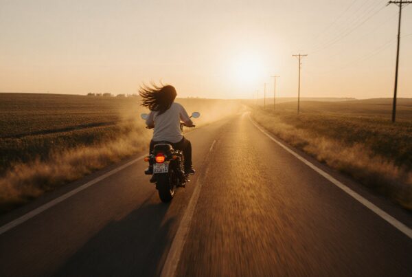 A motorcyclist rides alone on an open road at sunset.