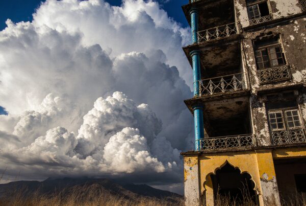 A towering cloud over an abandoned building with dramatic sunlight.