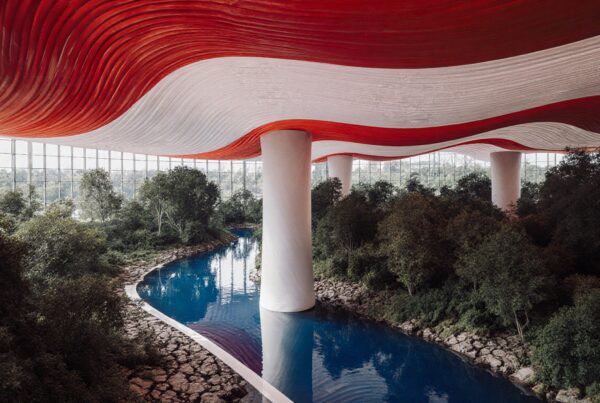 A beautiful indoor garden with a red and white undulating ceiling over a winding blue river, surrounded by lush greenery and tall columns.