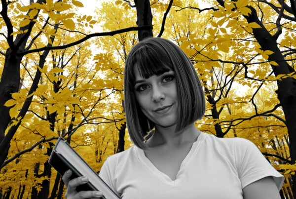 A grayscale woman holding a book stands in a forest of yellow autumn leaves.