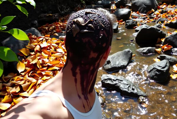 A person gazes at a stream surrounded by vibrant orange leaves, their head covered in a chocolate-like substance.
