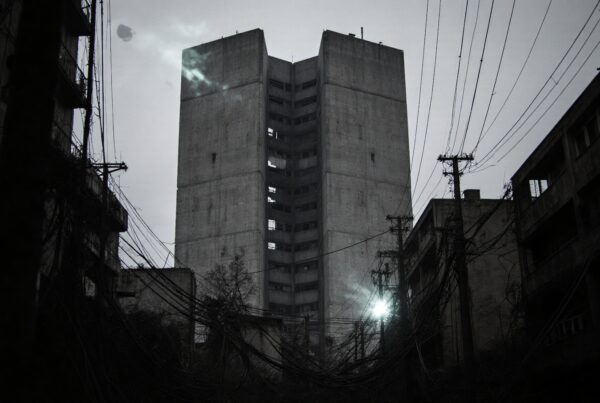 A tall, concrete building in an eerie, decaying urban environment with tangled wires.