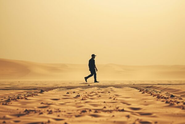 A lone figure walks across a tranquil, golden desert landscape at sunset.