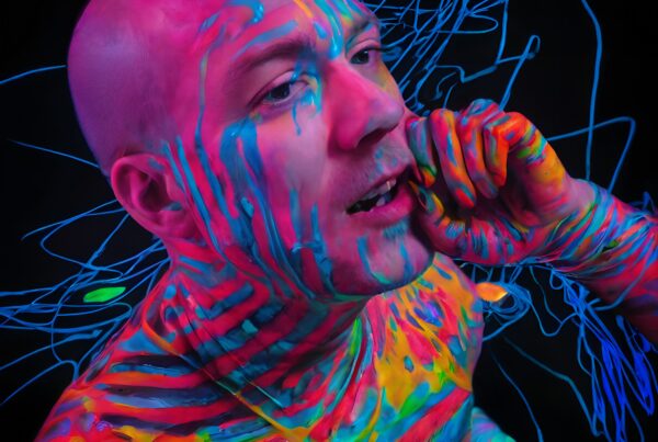 A person with vibrant UV-reactive body paint, glowing against a dark background.