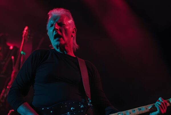 Musician performing energetically on stage with electric guitar in vibrant red and blue lighting.