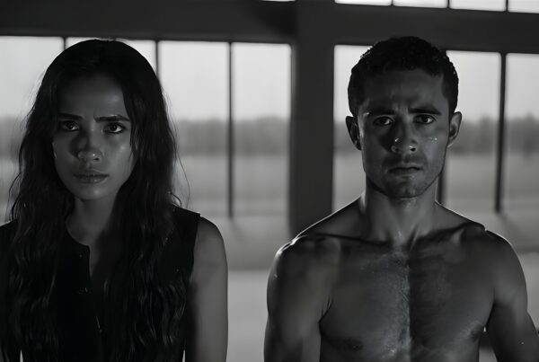 Two people with intense expressions stand in a dimly lit room with large windows.