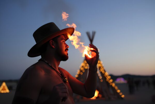 Man holding flame near teepee at festival during twilight with ethereal ambiance.