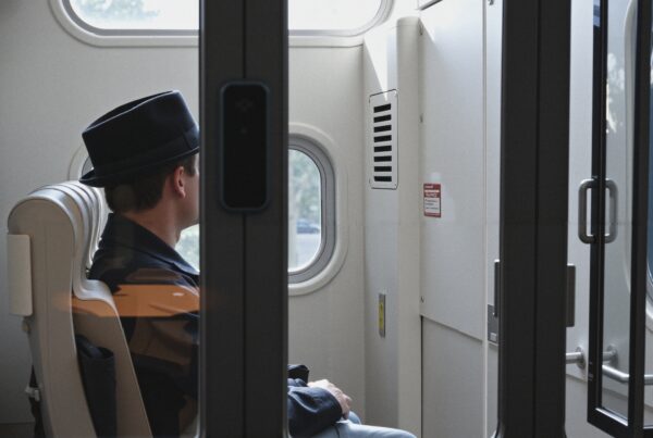 Man in hat sitting inside a modern train, gazing out the window.