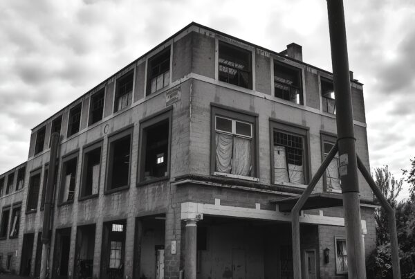 Abandoned industrial building with overcast sky, broken windows.