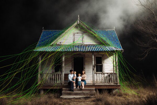 A family of four on the porch of an old house with threads draped over it.