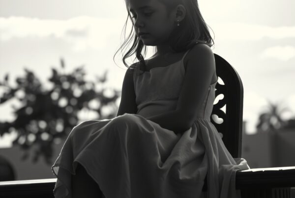 Monochrome portrait of a young girl sitting in contemplation on a wooden bench, with her silhouette backlit by sunlight and a serene natural background.