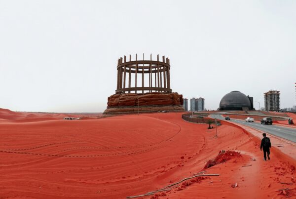 A red desert landscape contrasts with futuristic architecture and modern buildings under a stark sky.