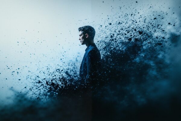 A man in profile dissolves into abstract particles in a blue-toned background, symbolizing transformation and introspection.