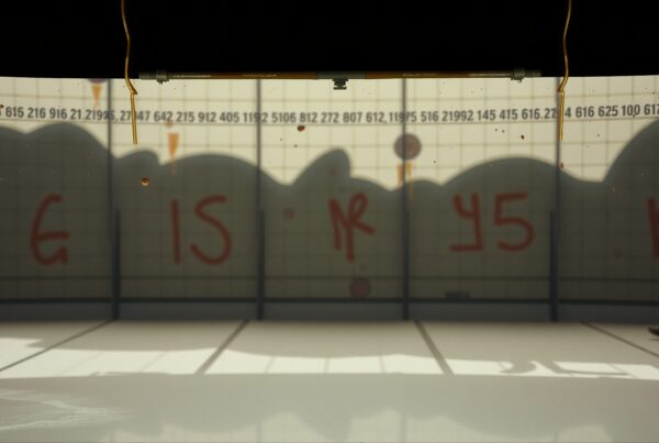 A man walks in front of a graffiti-covered wall with a grid pattern, casting shadows on the floor.