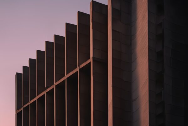 Modern building facade at twilight, showcasing geometric patterns and contrasting shadows against a pastel sky.