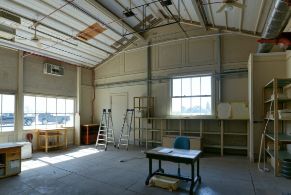 Spacious industrial-style room with large windows, metal ducts, and office furnishings.