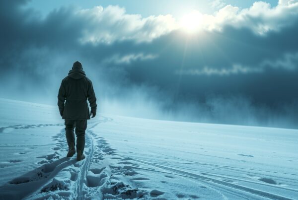 A lone figure walks on a snow-covered landscape under a cloudy sky with the sun shining through, creating a serene winter scene.