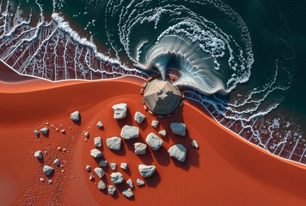 Aerial view of red sand beach with waves, rocks, and a stone gazebo.