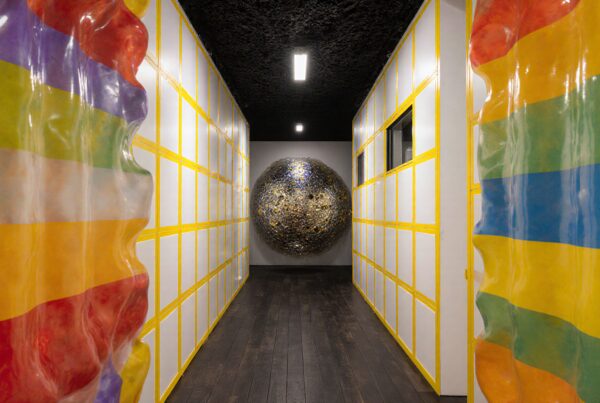 A narrow corridor with colorful rainbow-striped art installations and a textured spherical sculpture at the end.