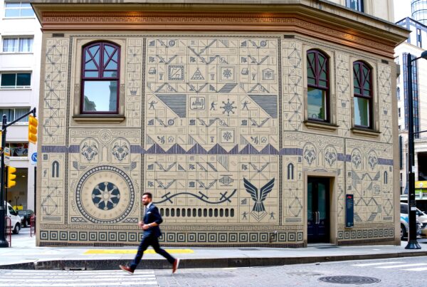 Exterior of a city building adorned with intricate geometric mural patterns and vibrant urban scenery.