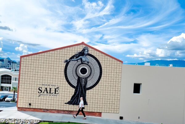 A large mural of a crowned woman on a building wall, under a dramatic cloudy sky, with a cityscape in the background.