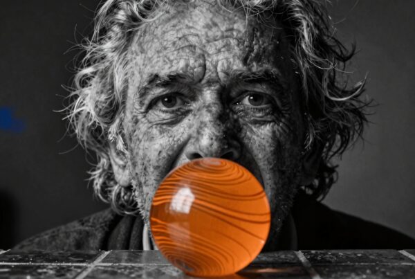 Elderly man observing an orange sphere in monochrome setting.