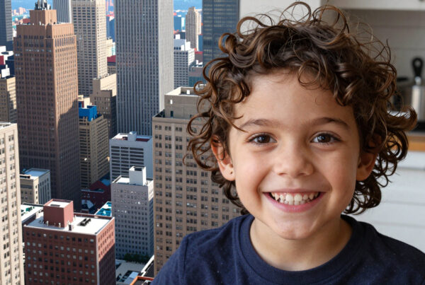 Cute smiling boy with curly hair posing inside apartment overlooking busy city skyline