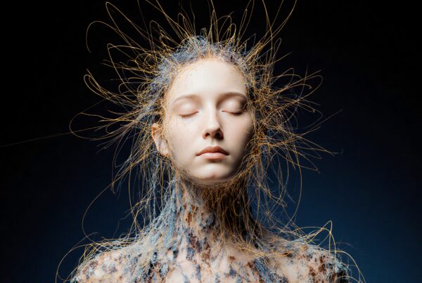 Mystical figure with web-like filaments in serene meditation against dark backdrop.