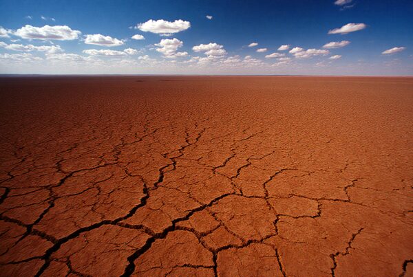 A cracked arid desert landscape stretches to the horizon under a blue sky with clouds.